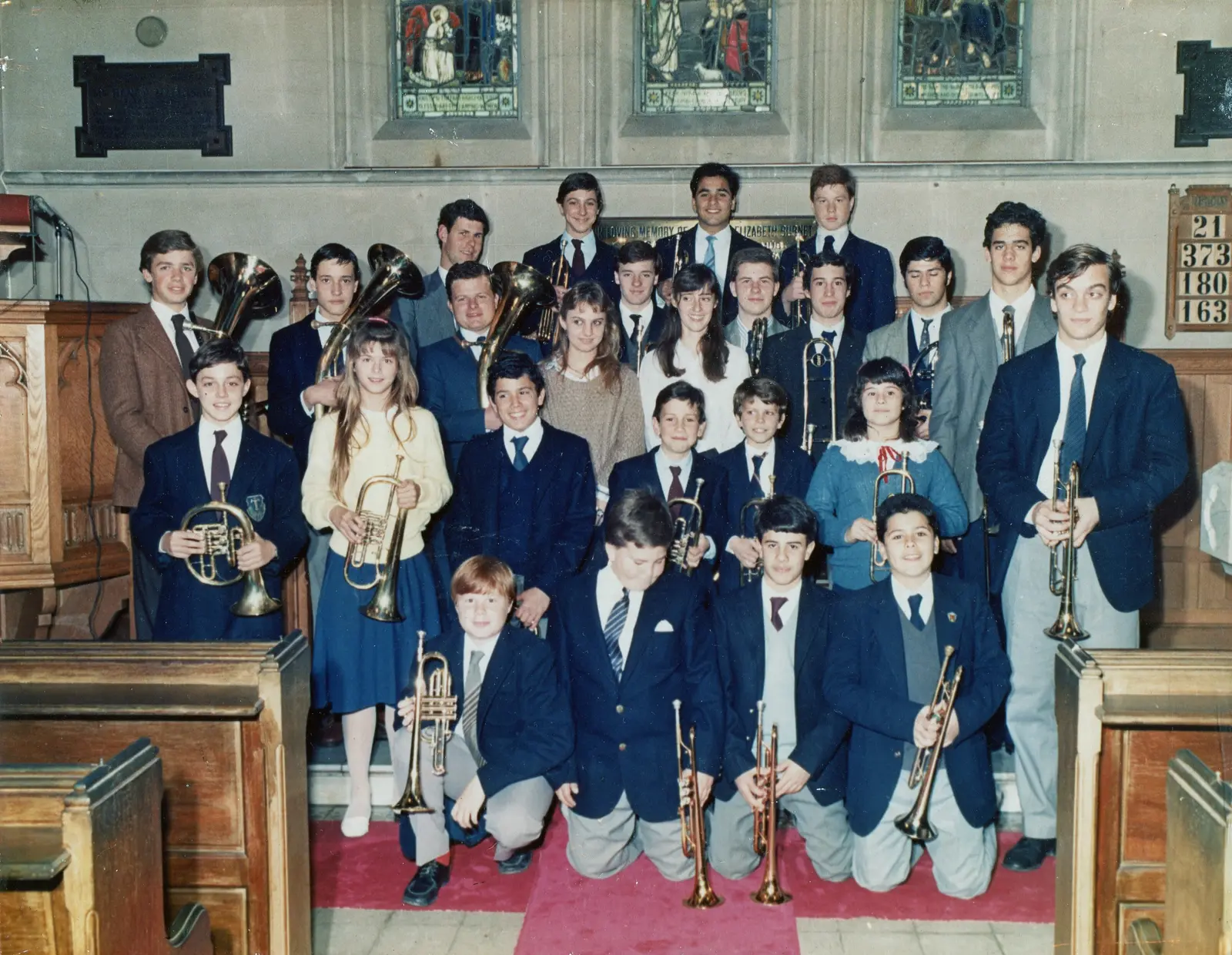 Foto grupal de unos veintiocho músicos del coro con sus instrumentos, en el interior de una iglesia con vitrales y tablero de himnos