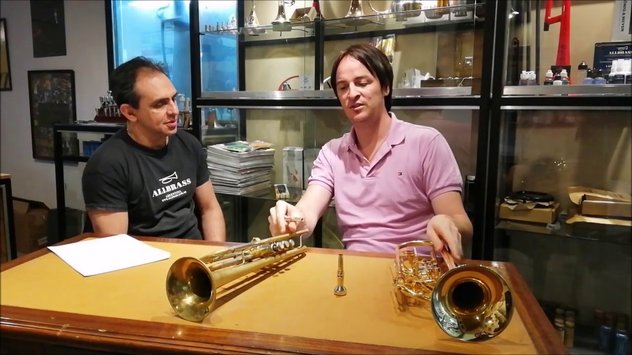 Daniel Crespo sentado en el taller All Brass junto al luthier, con dos trompetas doradas y una boquilla sobre la mesa