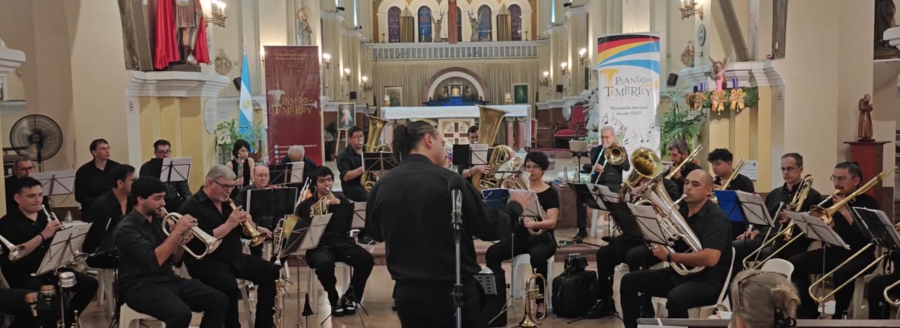 Die vollständige Besetzung des Posaunenchor Temperley beim Spiel im Altarraum einer Kirche, der Dirigent in der Mitte mit dem Rücken zur Kamera und das Banner des Chores im Hintergrund