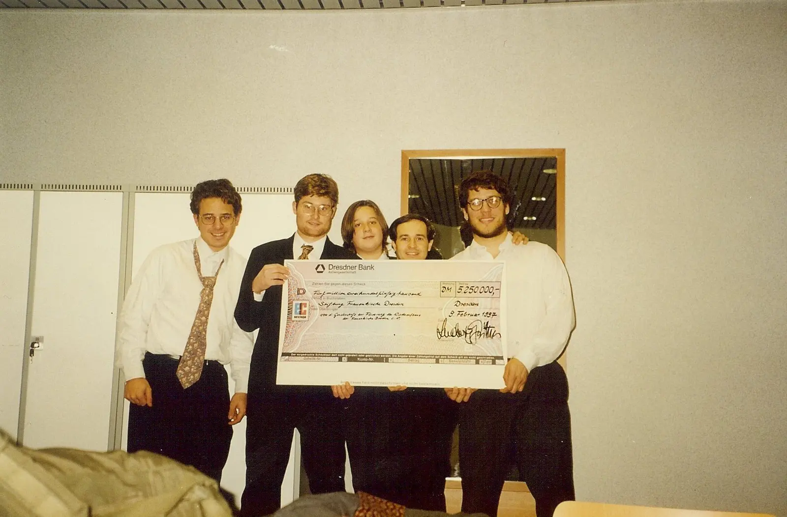 Cinco jóvenes de camisa y corbata sosteniendo un cheque gigante del Dresdner Bank por 5.250.000 marcos a nombre de la Stiftung Frauenkirche Dresden