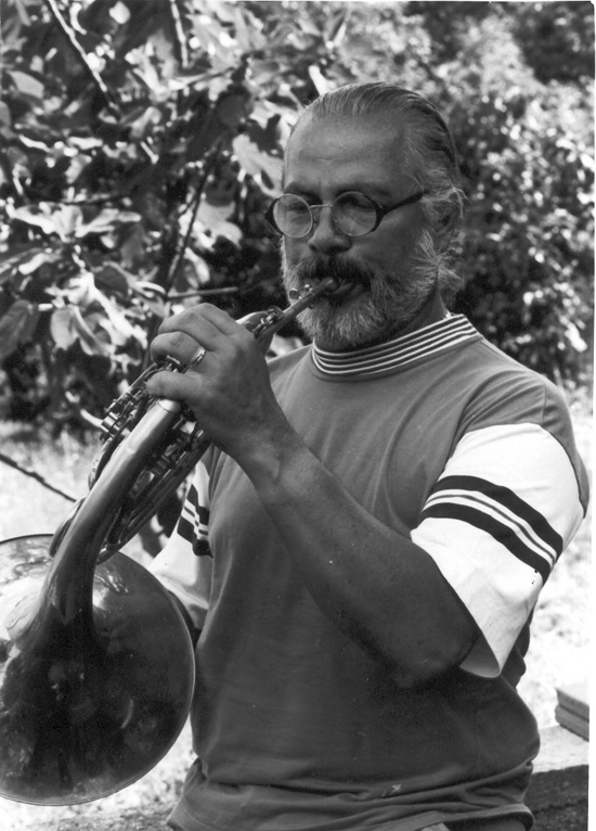 Fotografía en blanco y negro de Güelfo Nalli en sus últimos años, con barba, anteojos y remera deportiva, tocando al aire libre entre el follaje