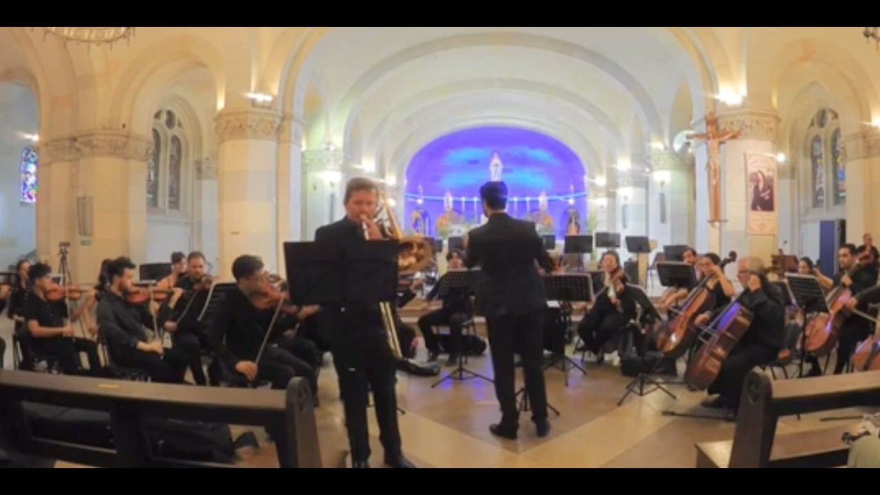 Willi Mengel como solista de la Rapsodia de Ewazen, de pie ante una orquesta de cuerdas en una iglesia