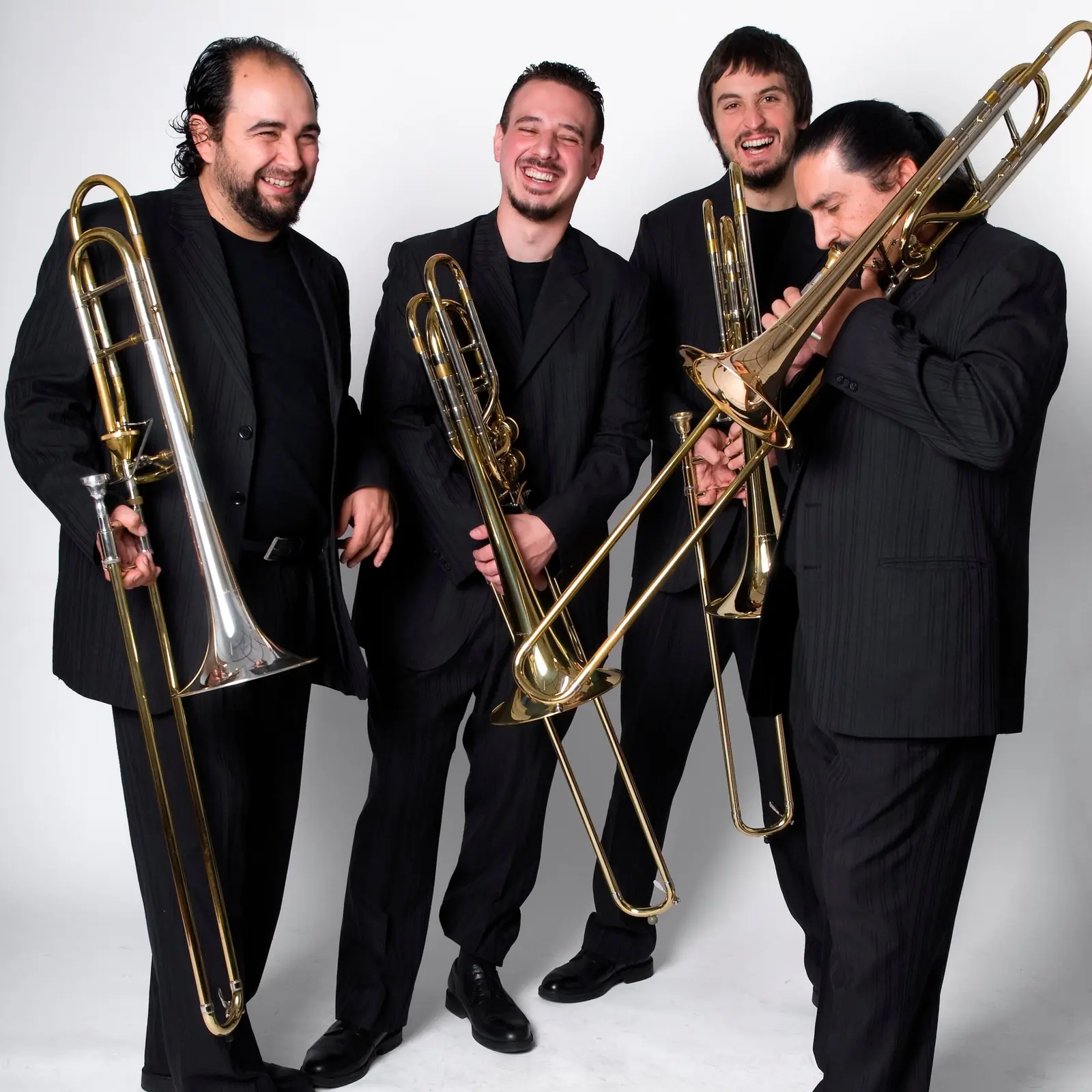 Los cuatro integrantes de Viento Sur Trombones riendo, con sus trombones, sobre fondo blanco