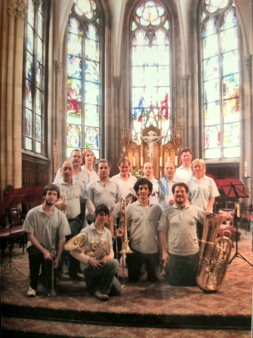 Catorce integrantes de la gira con la chomba celeste posando frente al altar de una iglesia gótica, con vitrales altos detrás y una bandera argentina sobre el hombro de uno de ellos
