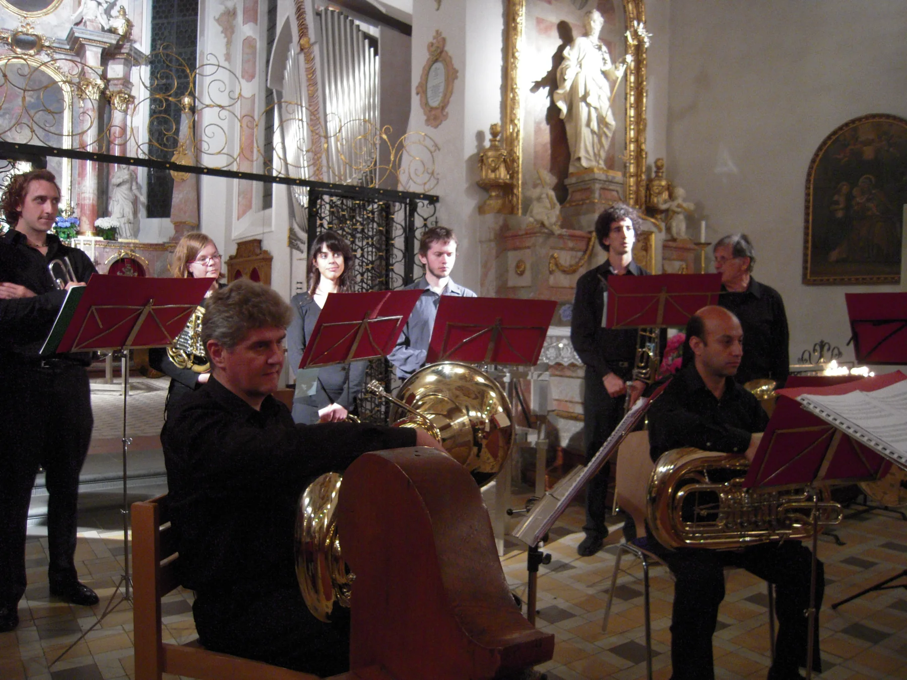 Músicos de negro tocando con atriles rojos dentro de una iglesia barroca de Pfullendorf