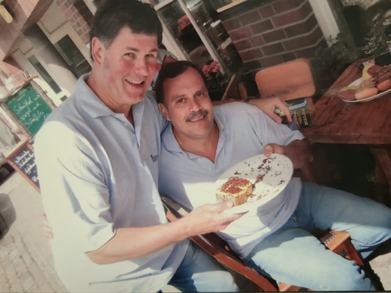 Dos integrantes de la gira con la chomba celeste, sentados en la vereda de un local, sostienen entre los dos un plato con un trozo de torta ya empezado