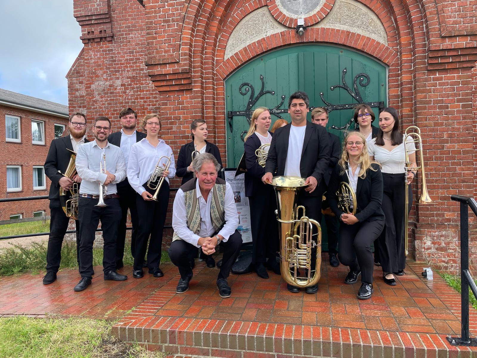 El conjunto reunido con sus instrumentos frente al portal de ladrillo rojo de una iglesia
