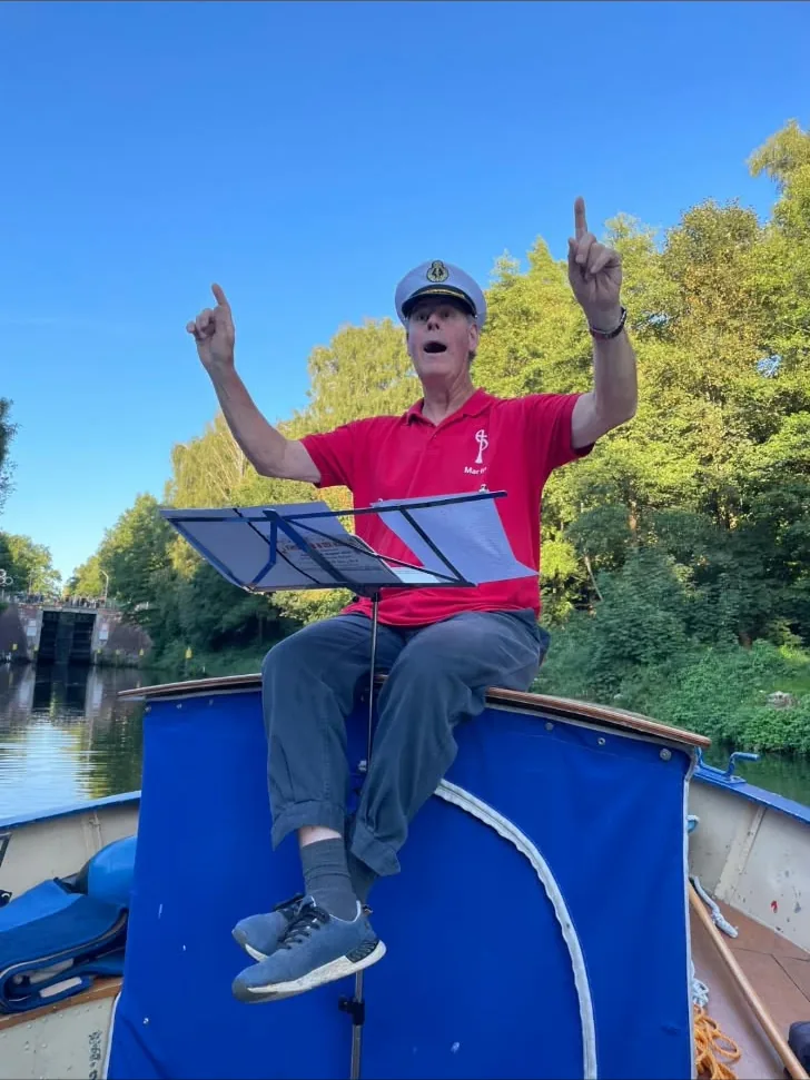 Martin Huss dirigiendo sentado sobre la cubierta de un barco, con gorra de capitán, en la esclusa de Bobzin