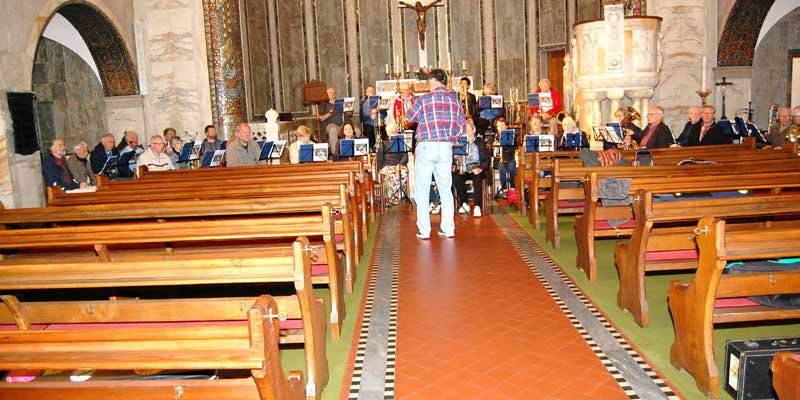 Interior de la Christuskirche de Roma con bancos de madera y el grupo ensayando al fondo de la nave