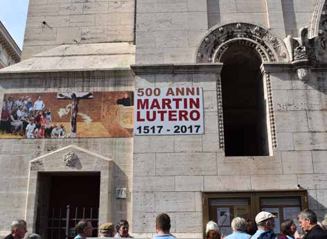 Fachada de una iglesia romana con una lona que dice 500 ANNI MARTIN LUTERO 1517-2017 y gente en la puerta