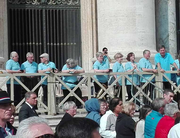 El conjunto apoyado en la valla de madera de la plaza, con público delante y la columnata detrás