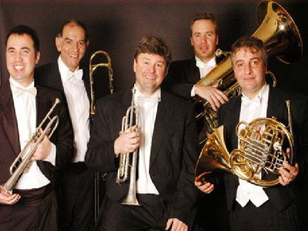 Studioporträt des Quinteto Bronces del Plata im Frack vor dunklem Hintergrund: zwei Trompeten vorn, Posaune hinten links, Horn rechts und der Tubist im Hintergrund auf eine große Tuba gestützt