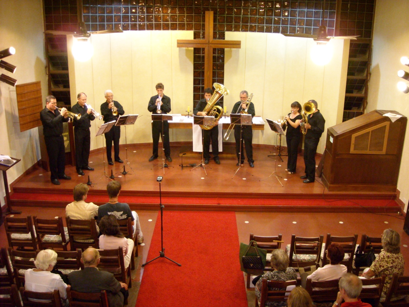 Olivos Brass tocando en una iglesia, frente a un altar con una cruz de madera