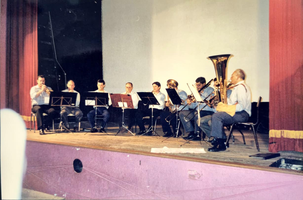 Nueve músicos tocando sentados sobre el escenario de un cine, entre cortinas rojas