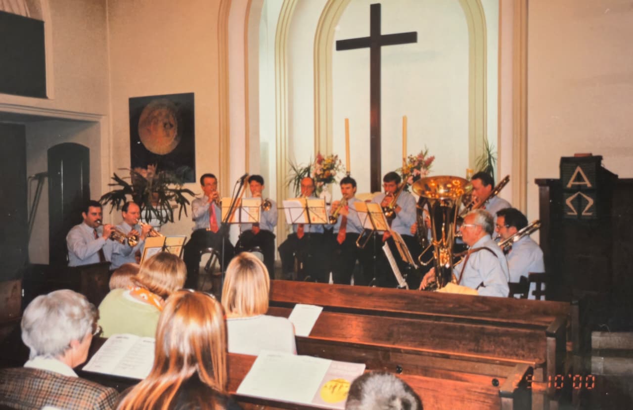 El coro tocando frente al altar de una iglesia con una gran cruz de madera, ante el público en los bancos