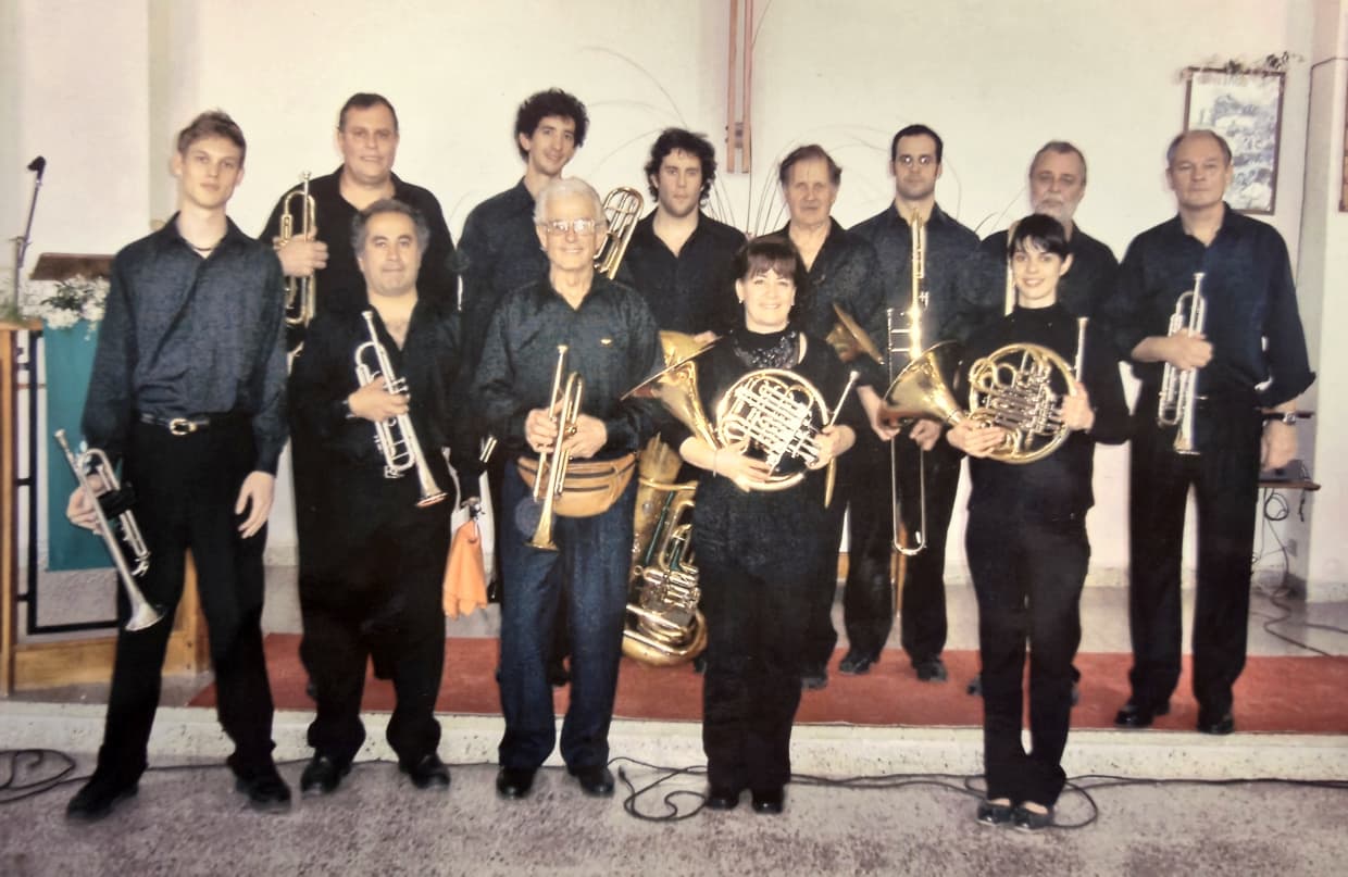 Doce músicos vestidos de negro posando con sus instrumentos frente al altar de una iglesia