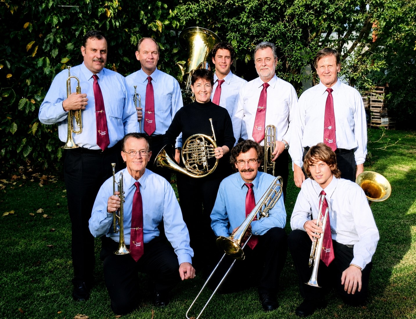 Nueve músicos de camisa celeste y corbata bordó posando con sus instrumentos en un jardín