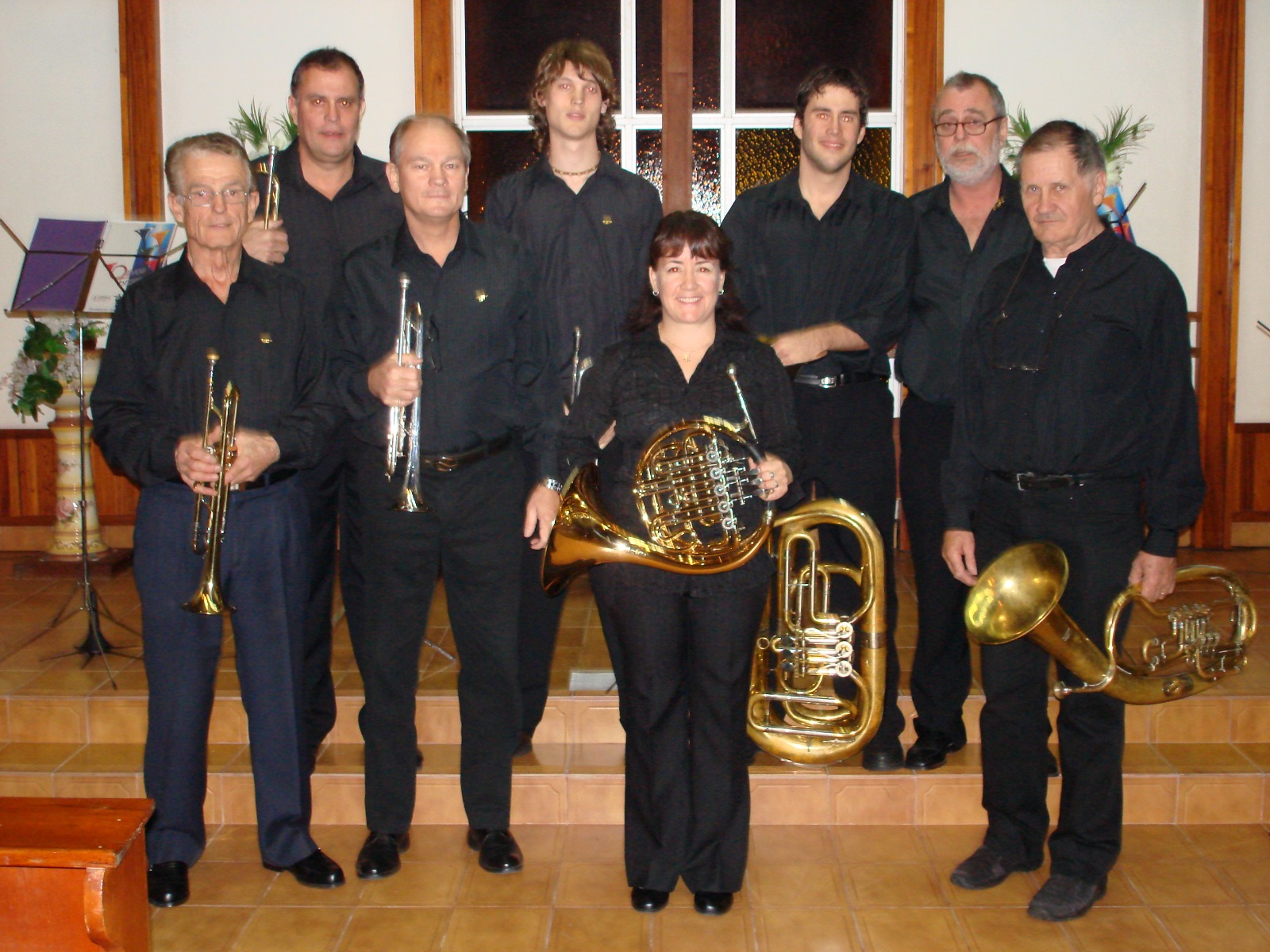Nueve músicos vestidos de negro posando con sus instrumentos en el presbiterio de una iglesia