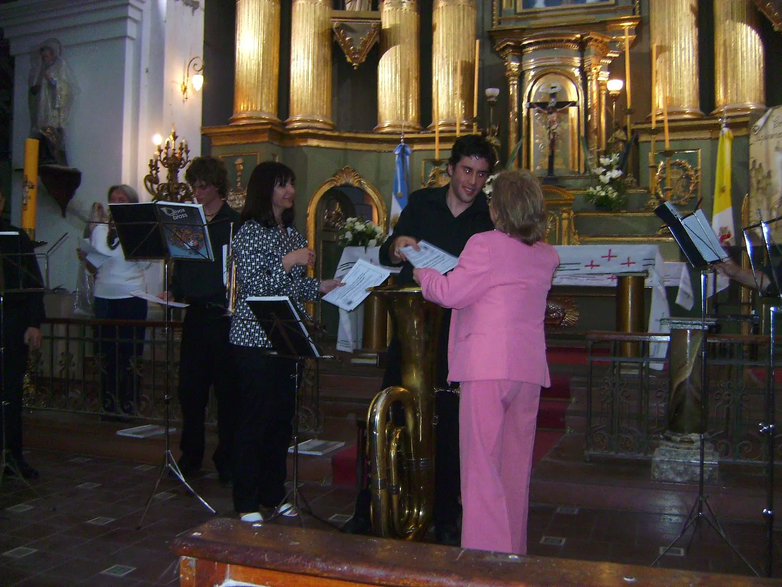 Una señora de rosa entrega diplomas a los músicos frente al altar dorado