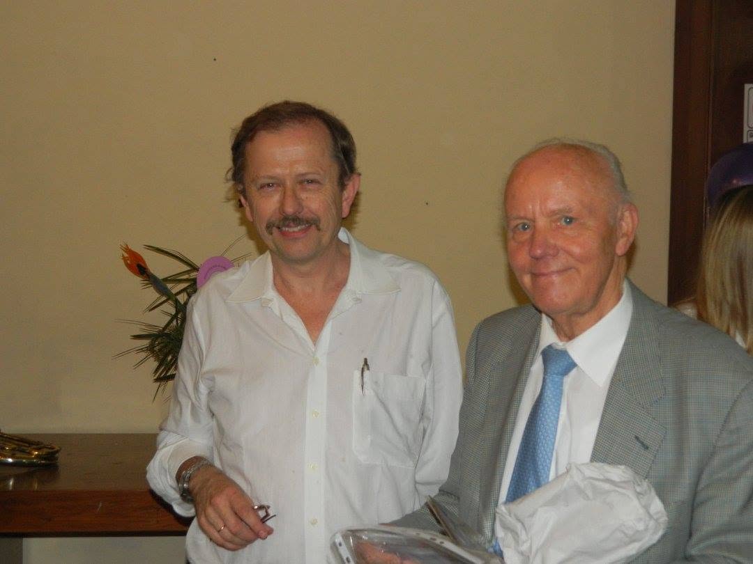 Dos hombres posan sonriendo: Herbert Luschnat, de camisa blanca y bigote, y a su lado Knud Autzen, de traje gris, sosteniendo un paquete envuelto en papel