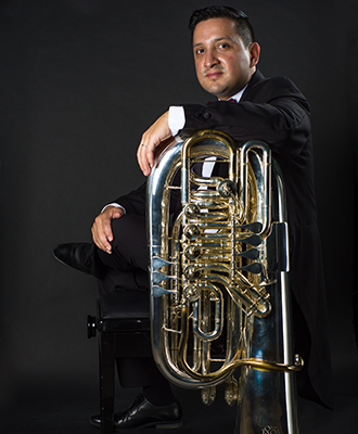 Retrato oficial de Richard Alberto Alonso Díaz de frac, apoyado sobre su tuba dorada, sobre fondo negro