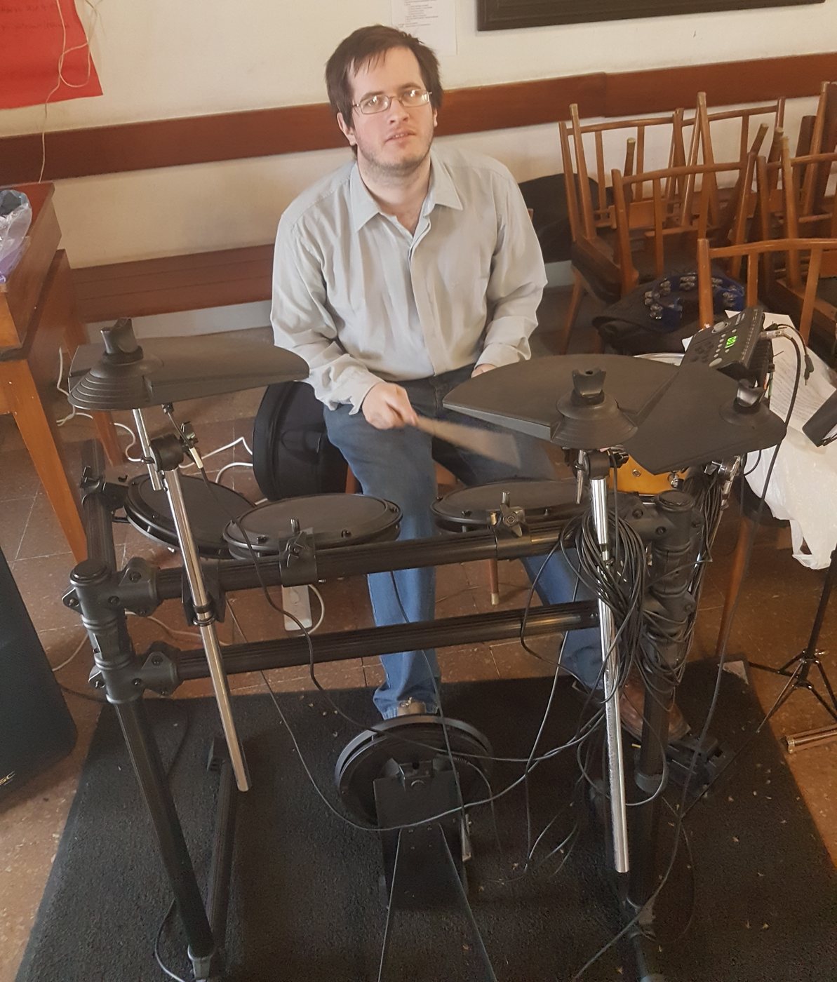 Werner Mengel toca una batería electrónica en el salón del coro en Temperley, con un bordado alemán enmarcado en la pared