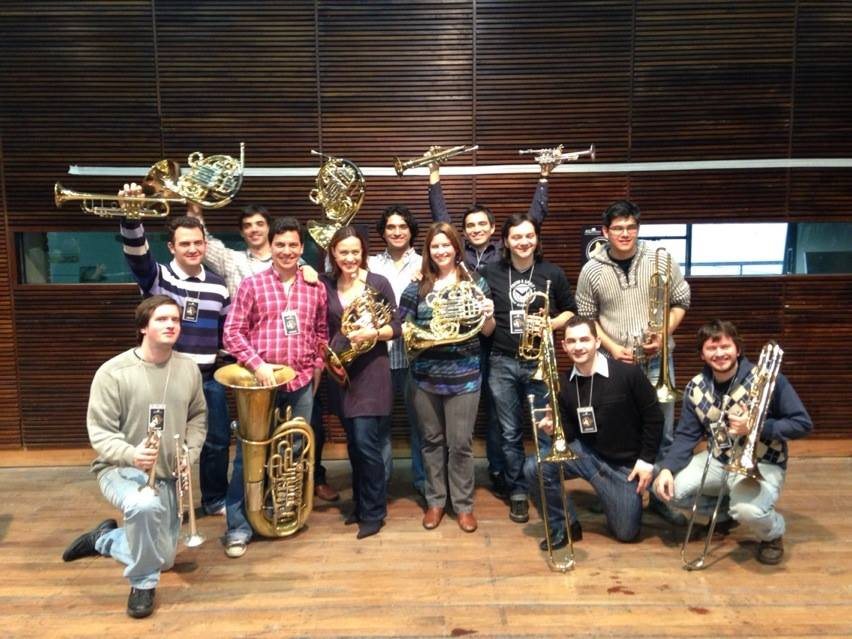 Grupo de jóvenes músicos de bronces levanta sus instrumentos junto a Sarah Willis, cornista de la Filarmónica de Berlín