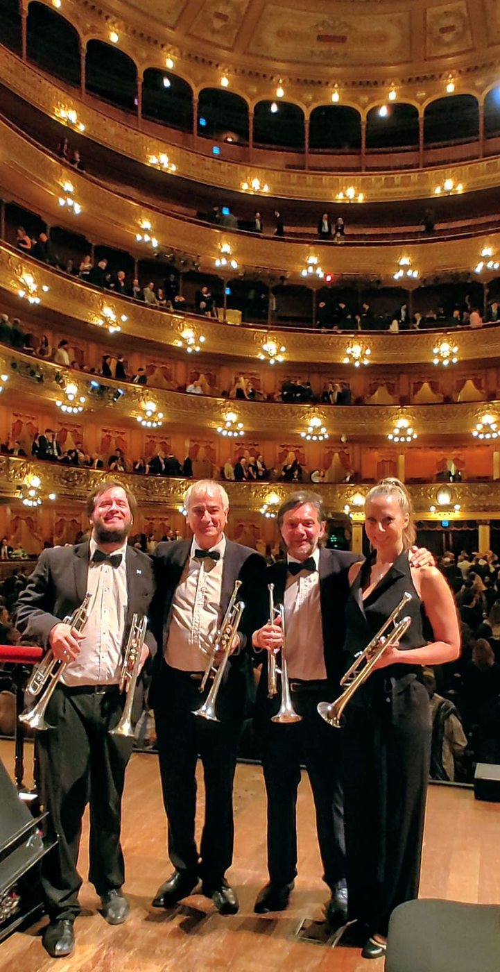 Cuatro trompetistas de frac posan en el escenario del Teatro Colón con la sala llena a sus espaldas