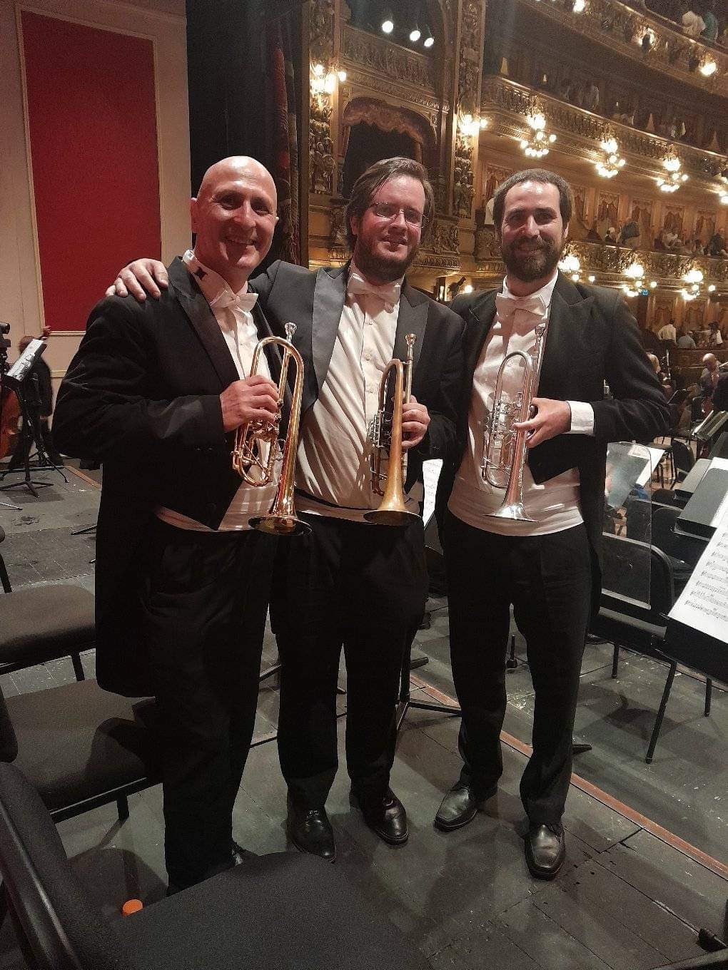 Tres trompetistas de frac y moño blanco posan en el escenario del Teatro Colón tras una función