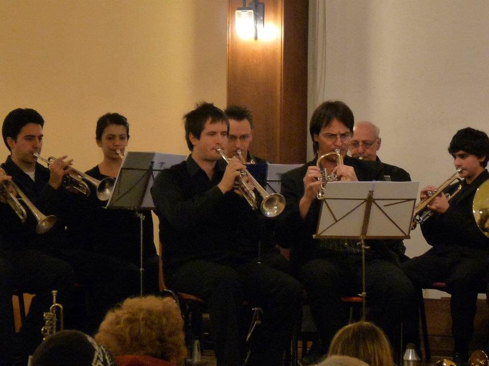Fila de trompetas y fliscornos de negro tocando en un concierto de bronces