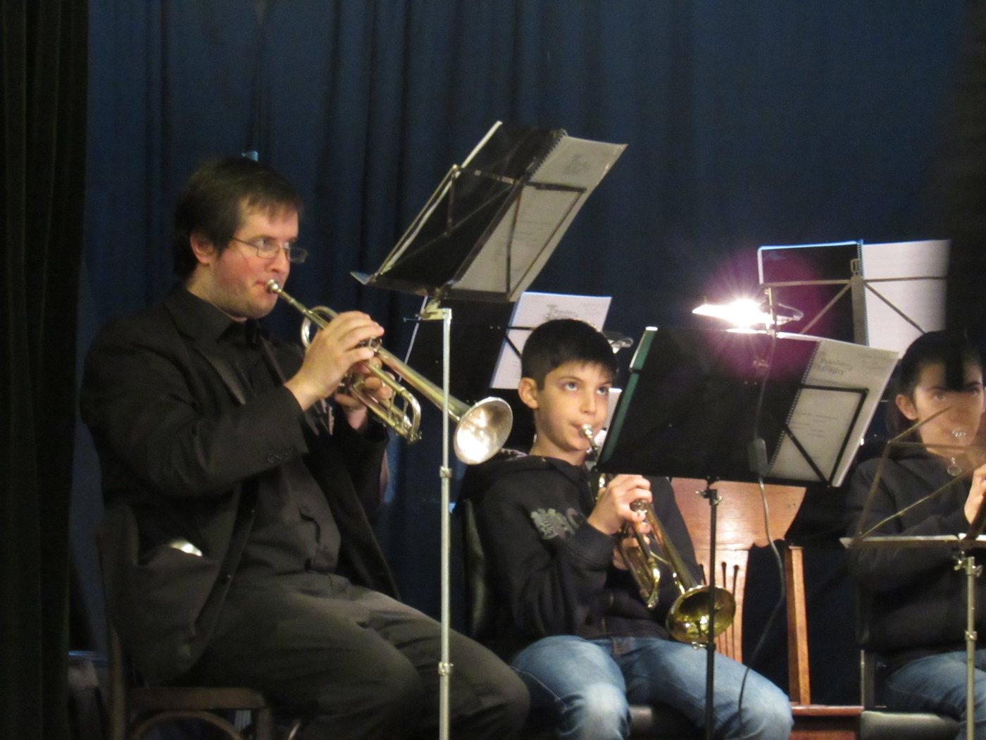 Werner Mengel toca la trompeta junto a un trompetista niño en un concierto del coro con telón azul