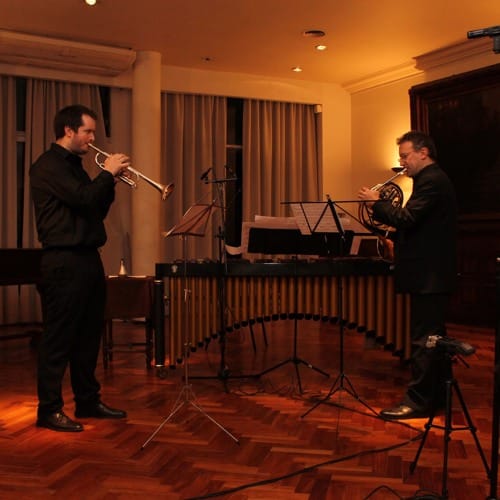 Werner Mengel toca la trompeta en dúo con un cornista en un concierto de cámara, con una marimba al fondo