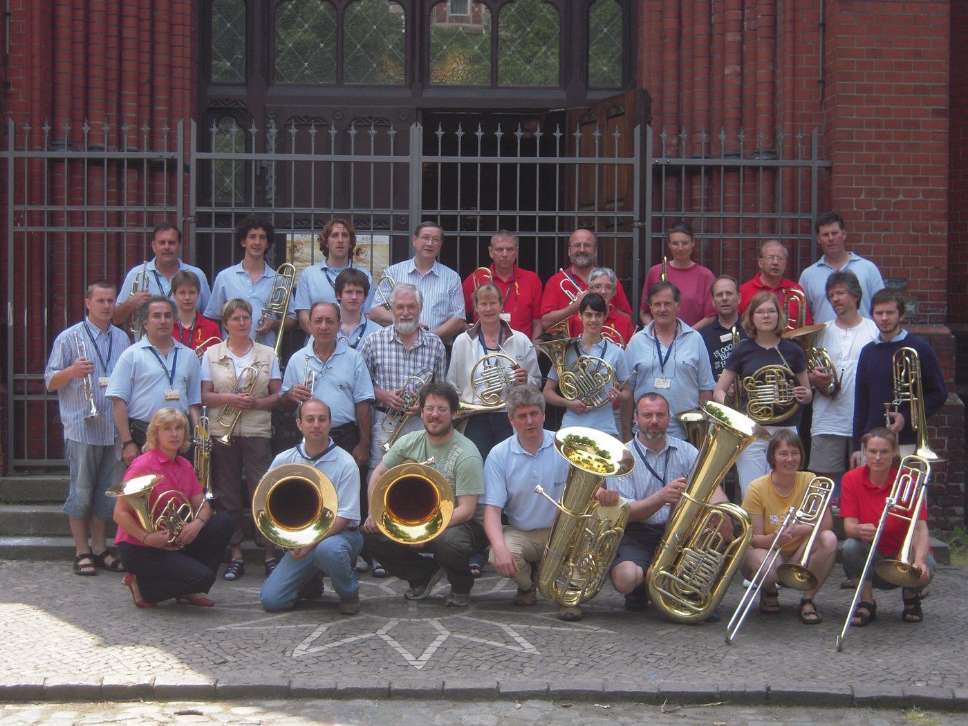 Numeroso grupo de músicos de bronces argentinos y alemanes posa con sus instrumentos ante una iglesia de ladrillo