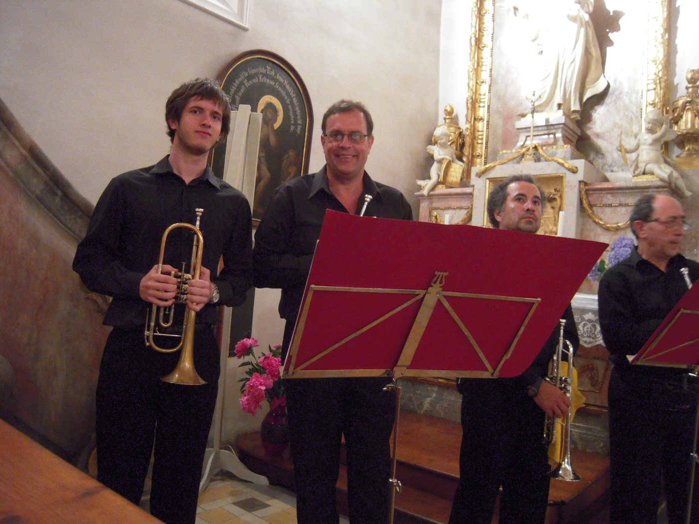 Cuatro músicos de negro posan con sus trompetas en el presbiterio dorado de una iglesia barroca alemana