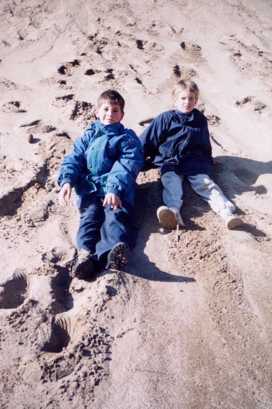 Dos chicos abrigados sentados en un médano de arena, foto familiar de los años noventa