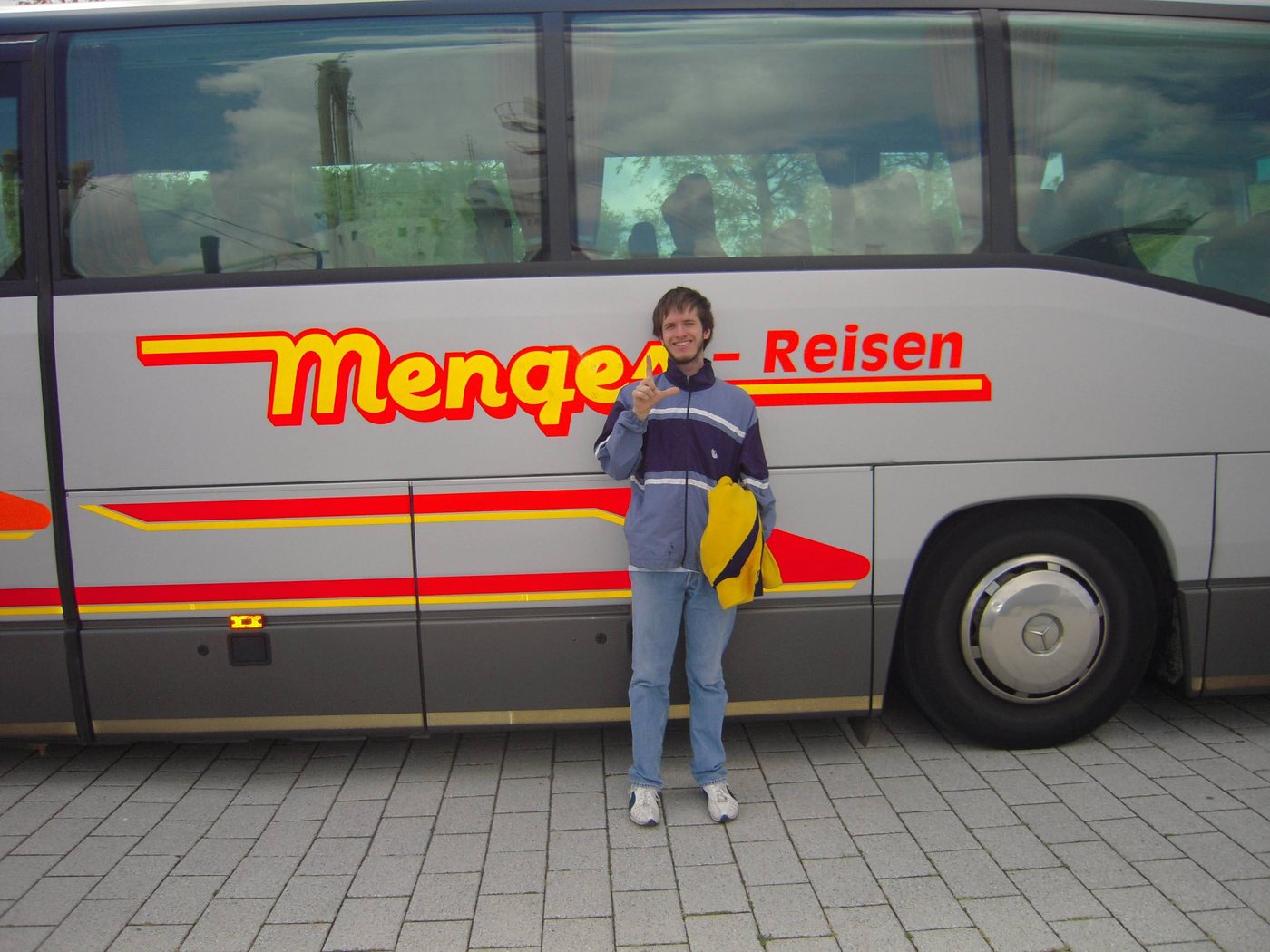 Werner Mengel tapa con el dedo la ese del cartel del bus Menges-Reisen para que se lea Mengel