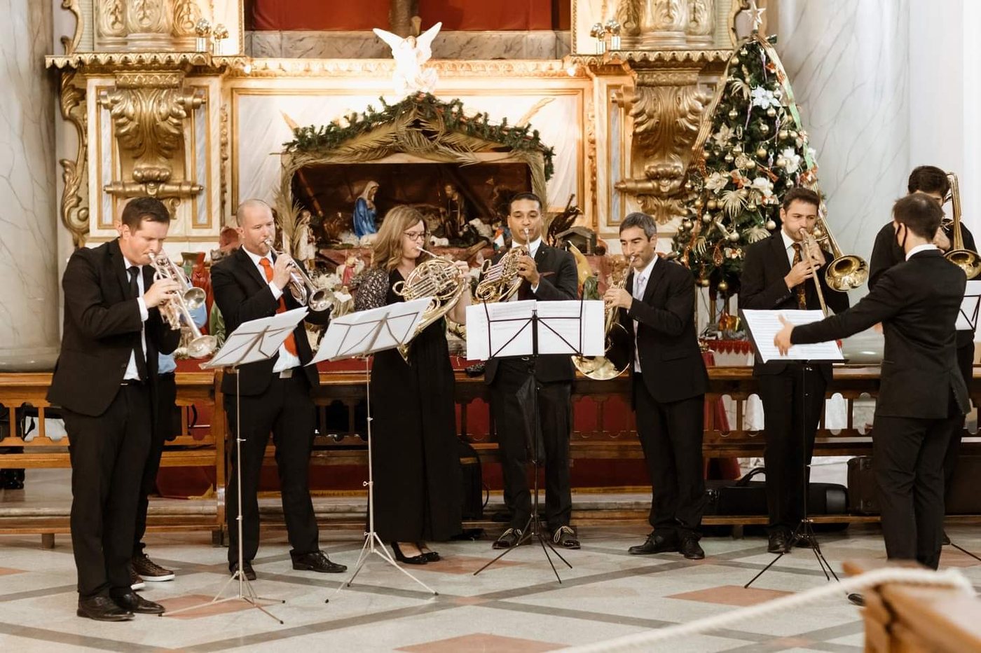 Ensamble de bronces toca frente al pesebre y el árbol de Navidad de una iglesia