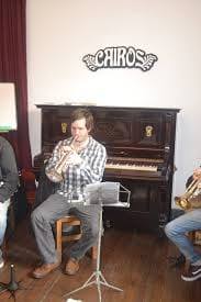 Werner Mengel toca la trompeta piccolo junto a un piano vertical en un café cultural