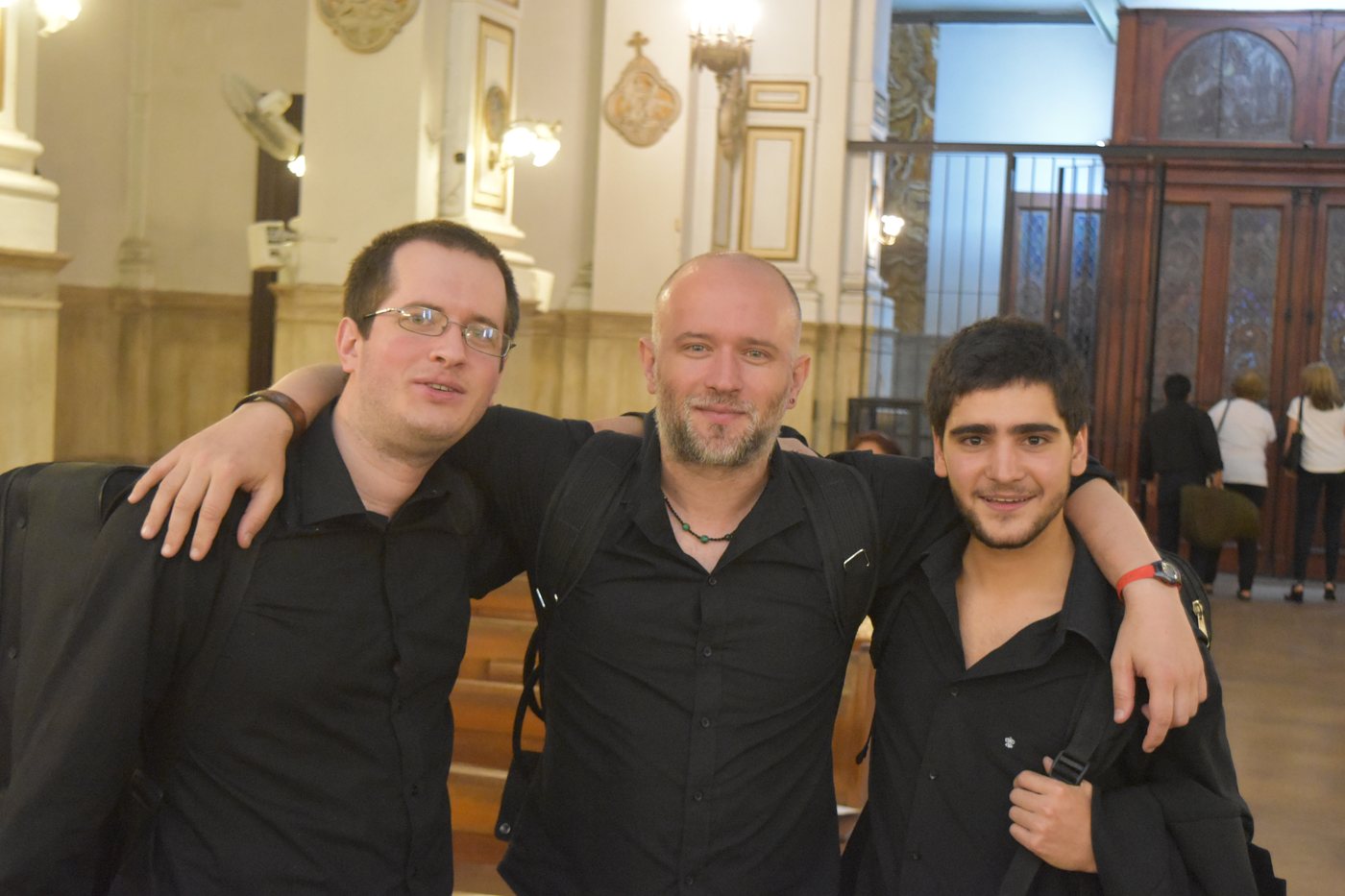 Tres músicos de negro se abrazan sonrientes en el interior de una iglesia después de un concierto